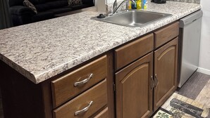 A kitchen with wooden cabinets, a granite countertop, and a dishwasher. - 1085 Cozy 1 Bedroom Condo on Mobile Bay (Daphne)