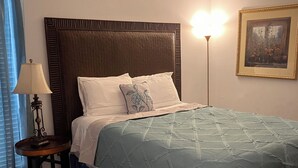 A neatly made bed with a blue and white quilt, a wooden headboard, and a bedside lamp. - 1085 Cozy 1 Bedroom Condo on Mobile Bay (Daphne)