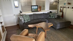 Un salón con un sofá seccional gris, una mesa de centro de madera y un sillón de cuero color arena.