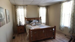 A bedroom with a wooden bed, two bedside tables, a nightstand, and a window with curtains. - Charming House with Amazing Views! Next to Marina and Tiki Bar (Lansing)