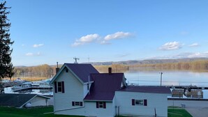 A two-story house with a dark roof, situated by a lake with boats docked nearby. - Charming House with Amazing Views! Next to Marina and Tiki Bar (Lansing)