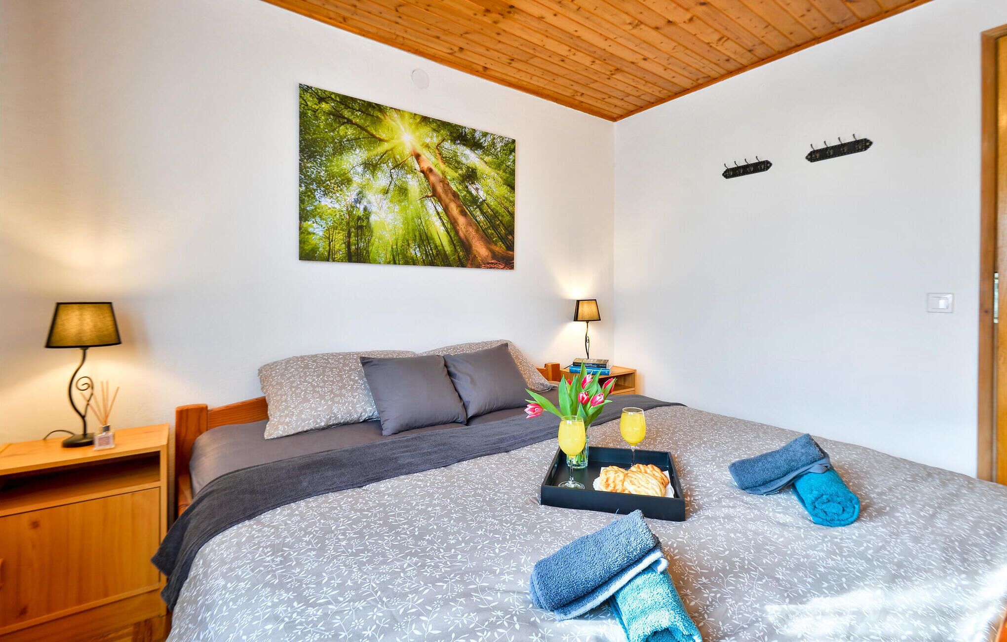 A neatly arranged bedroom with a bed, a bedside table, a lamp, a tray with breakfast items, and a painting on the wall.