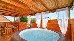 Une terrasse en bois avec un jacuzzi, des meubles en bois et un espace patio couvert.