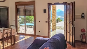 A room with a sofa, a table with chairs, a sliding glass door leading to an outdoor area with a table and chairs, and a stone wall. - Stunning home in El Jaral (El Jaral)