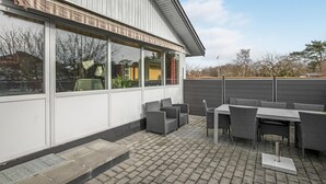 An outdoor patio area with a table and chairs, a covered seating area, and a view of a building with large windows. - Gorgeous home in Nexø with WiFi (Nexø)