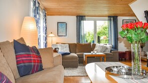A cozy living room with a sofa, a coffee table, and a lamp. There is a window with curtains and a vase with flowers on the table. - 7 bedroom awesome home in örkelljunga (Örkelljunga)