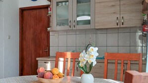 Uma cozinha com armários de madeira, painel de azulejos, mesa de madeira com uma fruteira, vaso com flores e tábua de corte.