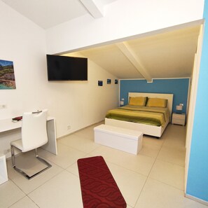 Ein Schlafzimmer mit einem Bett, einem Schreibtisch, einem Sessel, einem Fernseher und einem roten Teppich.