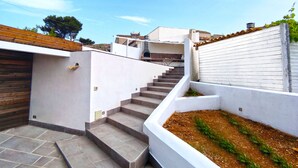 Een moderne buitenstairtrap die leidt naar een dak terras met een witte muur en een kleine tuin.