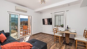 Un salon moderne avec un canapé noir, une table à manger dressée pour deux personnes et un balcon offrant une vue agréable.