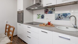 Une cuisine moderne avec des armoires blanches, une hotte de cuisinière en acier inoxydable, un four encastré, un évier et une planche à découper avec des légumes.