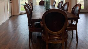 Ein geräumiger Speisesaal mit einem großen Holztisch und passenden Stühlen, einer Pendelleuchte sowie großen Fenstern mit Blick ins Freie.