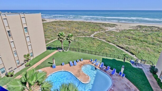 A pool area with a view of the beach and ocean, surrounded by a fence and palm trees. - Beach FRONT Hideaway for your Fun in the Sun!️ (South Padre Island)