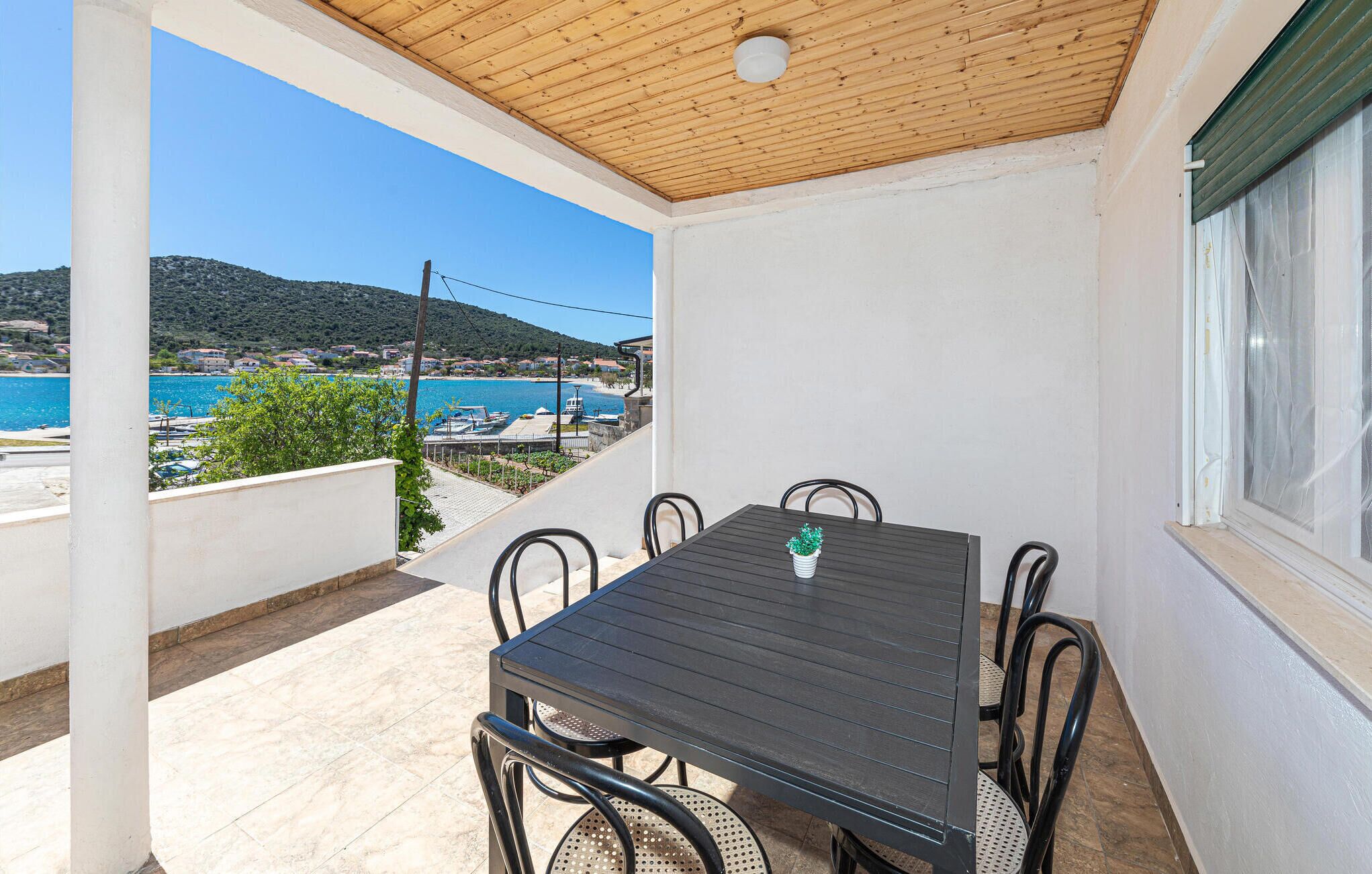 A covered outdoor patio with a table and chairs, overlooking a coastal area with buildings and a body of water.