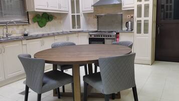 Una cocina con una mesa redonda de madera, cuatro sillas grises, armarios blancos, una estufa y un lavamanos.