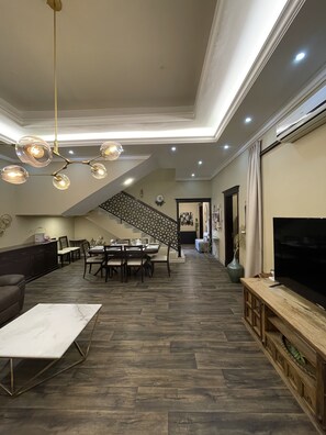 A spacious living room with a dining area, a staircase, and a TV on the right. - Kaleidoscope - Luxury 6 Bedroom villa in AJMAN (Ajman)