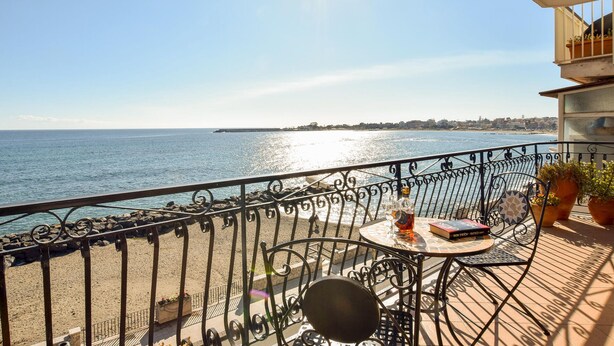 A balcony with a view of the sea, a table with a book, and potted plants. - Nice apartment in Giardini Naxos with WiFi (Giardini Naxos)