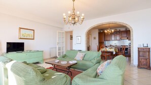 A living room with green sofas, a coffee table, a TV, and a chandelier. - Nice apartment in Giardini Naxos with WiFi (Giardini Naxos)