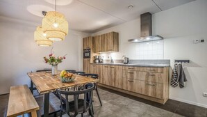 Eine moderne Küche mit Holzschränken, einer Edelstahlspüle und einem eingebauten Herd. Ein Essbereich mit Holztisch und -stühlen, darüber eine Pendelleuchte.