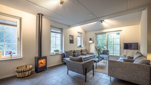 Ein modernes Wohnzimmer mit Kamin, grauen Sofas, einem Couchtisch und großen Fenstern.