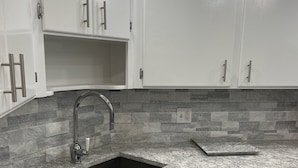 Una cocina con armarios blancos, encimera de granito, lavavajillas de acero inoxidable y salpicadero de azulejos.