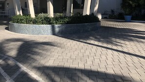 Un edificio moderno con entrada cubierta, varios pisos y un área ajardinada con plantas.