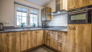 A modern kitchen with wooden cabinets, a built-in oven, and a window with blinds.
