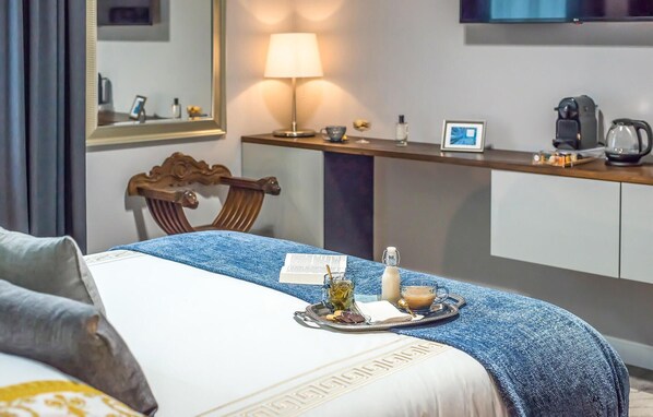 Une chambre d’hôtel avec un lit bien fait, une table de chevet avec une lampe, une machine à café et un plateau avec une tasse de café et une bouteille d’eau.
