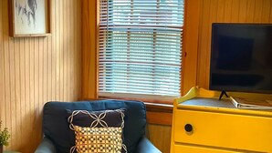 A room with a blue armchair, a yellow dresser, a television, and a window with blinds.