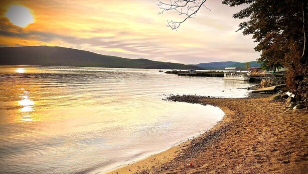 A beach with a curved shoreline, calm water, and a distant view of mountains.