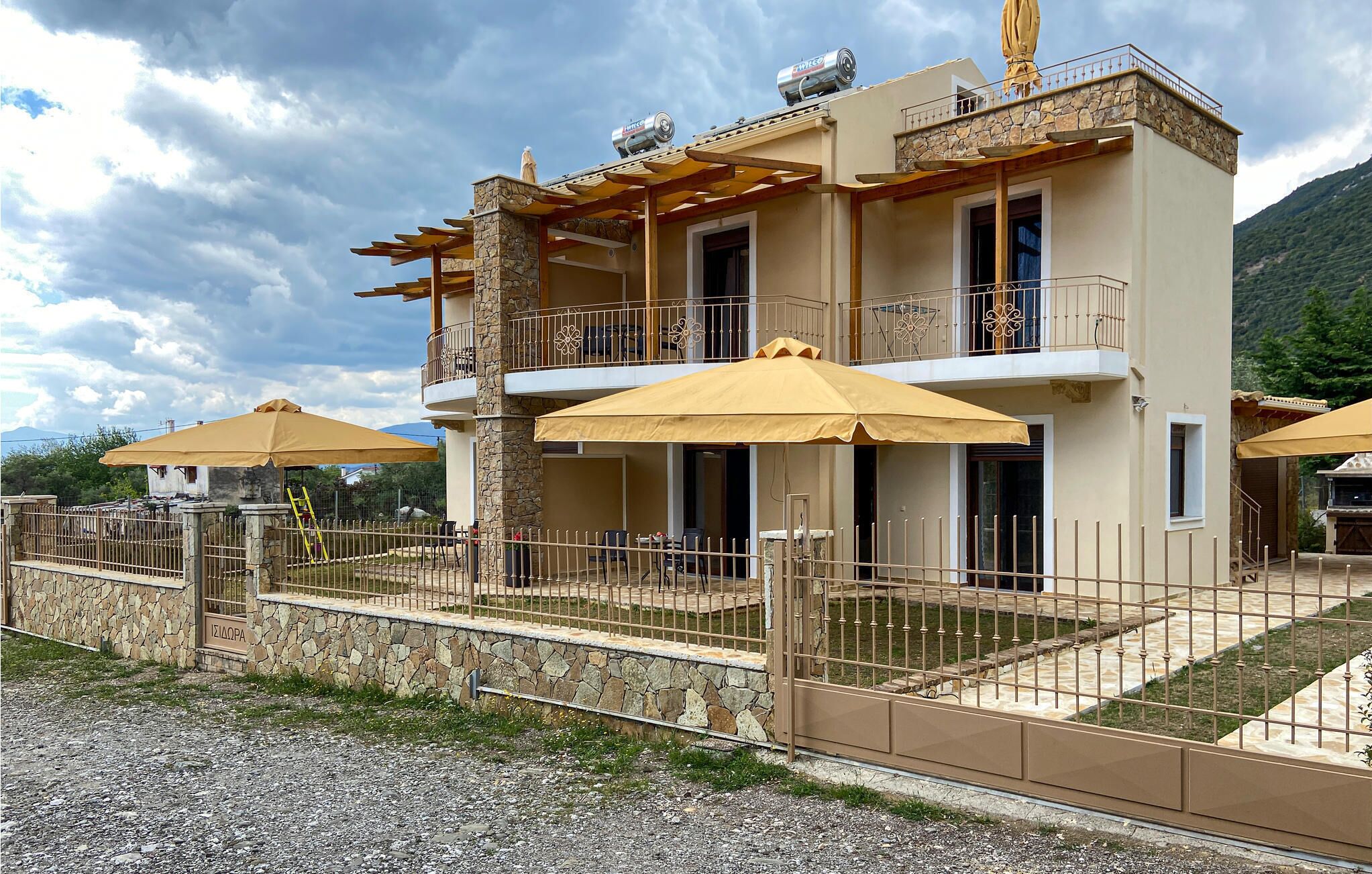 Un bâtiment à deux étages doté de balcons, d’espaces de détente en plein air avec des parasols et d’un mur en pierre.
