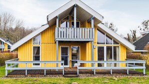 A yellow house with a balcony, large windows, and a wooden deck. - Nice home in Rechlin with sauna (Rechlin)