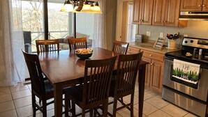 A dining area with a wooden table and chairs, a chandelier, and a kitchen with wooden cabinets and a stove. - Woodson Bend-Golf, Pool Restaurant& More-Near Burnside W/Lake View - First Floor (Bronston)