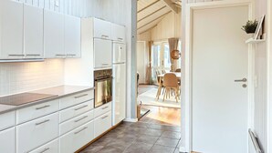 Una cocina moderna con muebles blancos, horno integrado y comedor con mesa y sillas.