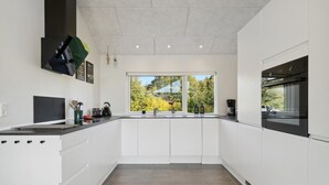 Une cuisine moderne avec des meubles blancs, un plan de travail noir et une fenêtre donnant sur la verdure à l’extérieur.