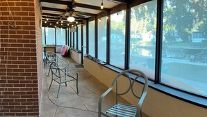 Un espacio al aire libre cubierto con sillas de metal, un muro de ladrillo y ventanas amplias con vistas a un estacionamiento.