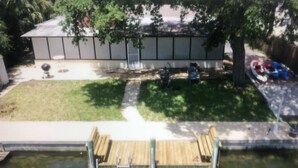 Un muelle de madera sobre un estanque, un césped y un edificio con patio cercado.