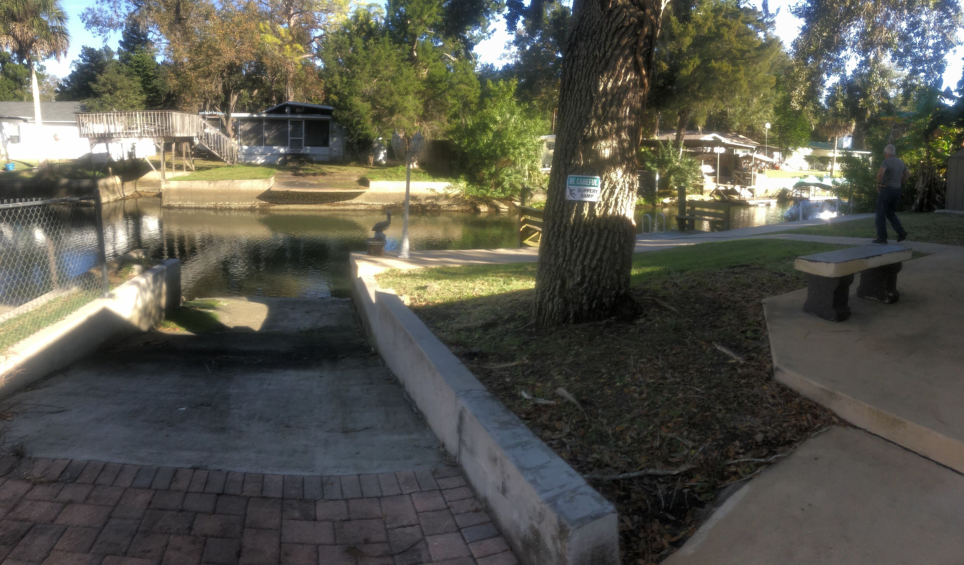A pond with a wooden walkway, a bench, and a sign indicating a 'BE CAREFUL RAMP'.