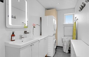 Une salle de bain moderne avec un lavabo blanc, un miroir et un lave-linge encastré.