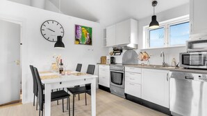A modern kitchen with white cabinets, stainless steel appliances, a dining table with chairs, a clock, and artwork on the wall. - Stunning home in Nexø with WiFi (Nexø)