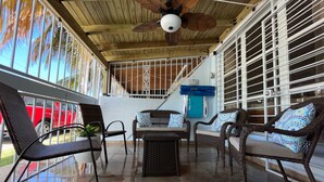 A covered patio area with wicker furniture, a ceiling fan, and a view of palm trees.