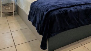 A neatly arranged bedroom with a bed, two bedside tables, a nightstand, a wall-mounted artwork, and a curtain.