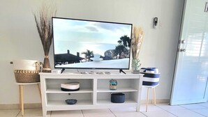 A living room with a TV on a white stand, a colorful rug, and a white ottoman.