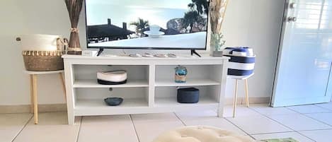 A living room with a TV on a white stand, a colorful rug, and a white ottoman.