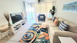 A living room with a TV, sofa, coffee table, and a colorful rug.