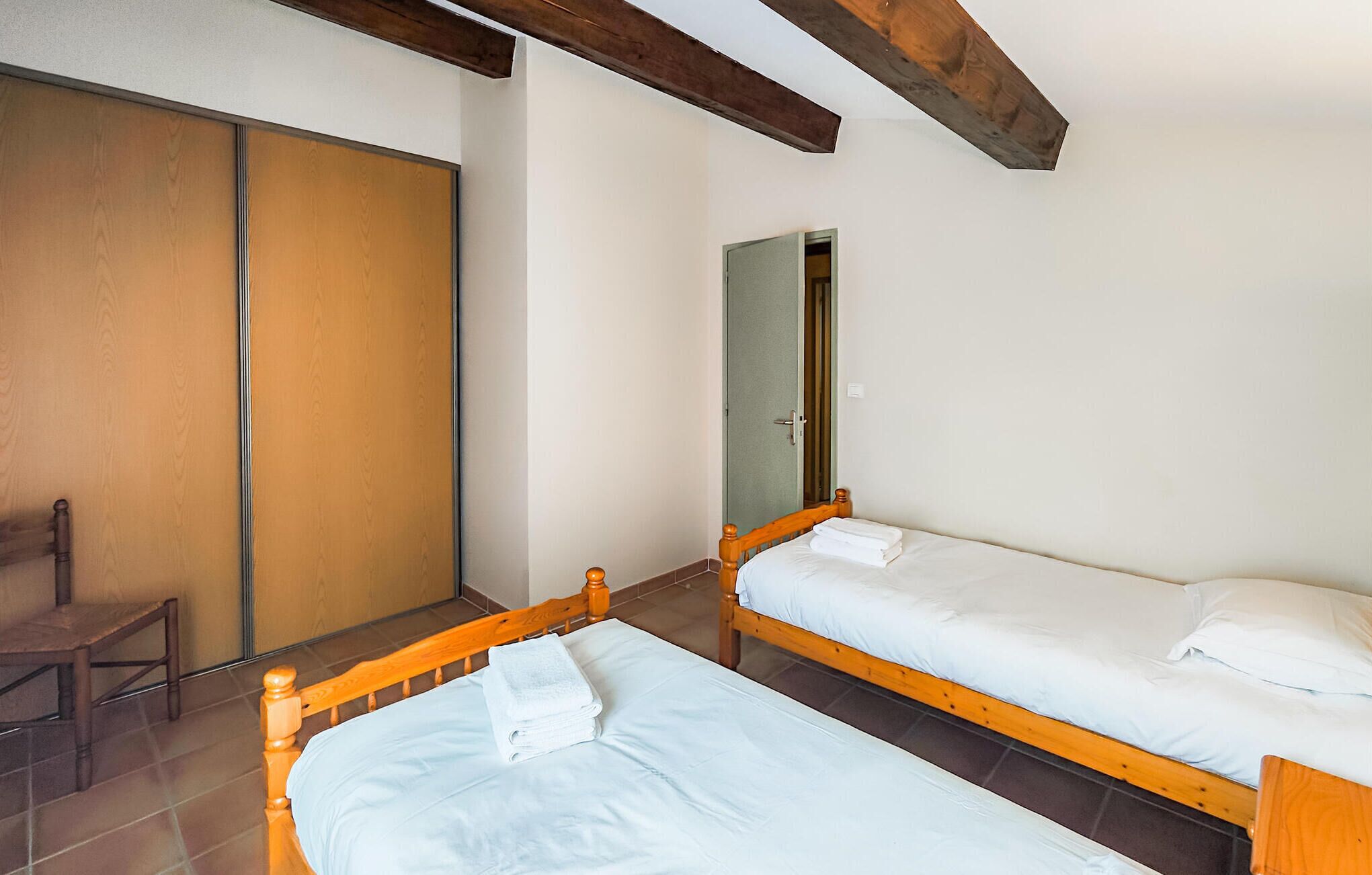 Un dormitorio con dos camas individuales, una silla de madera y un armario.
