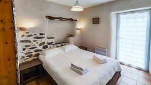 A bedroom with a stone wall, a bed with white linens, a small table, and a radiator. - Awesome home in Cabrerolles (Cabrerolles)