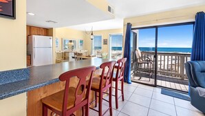 Una cocina con barra, sillas de madera y vistas a la playa a través de amplios ventanales.