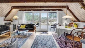 A cozy loft-style living room with a black leather sofa, a glass coffee table, and a dining area with a white tablecloth. - Lovely home in Rømø with kitchen (Rømø)