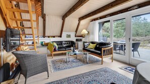 A spacious living room with a high ceiling, wooden beams, a black leather sofa, a wicker chair, a glass coffee table, and a large sliding glass door leading to an outdoor area. - Lovely home in Rømø with kitchen (Rømø)
